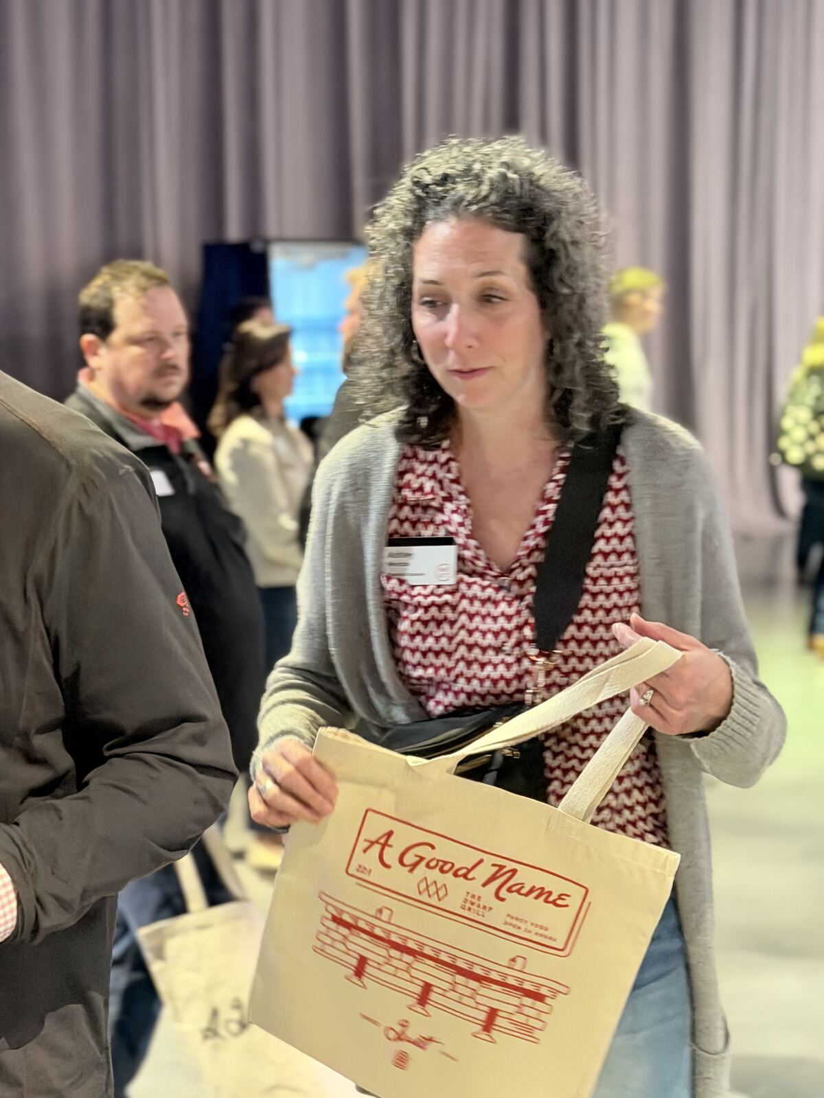 Woman displays a custom cream canvas tote with colorful embroidered florals at a conference booth